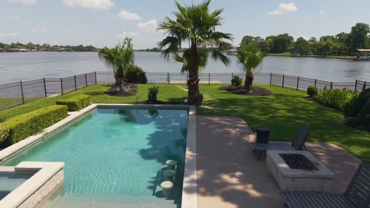 Aerial view of the backyard at 217 Lakeshore Dr: a swimming pool and spa, palm trees, a fire pit and a lawn running down to open water.